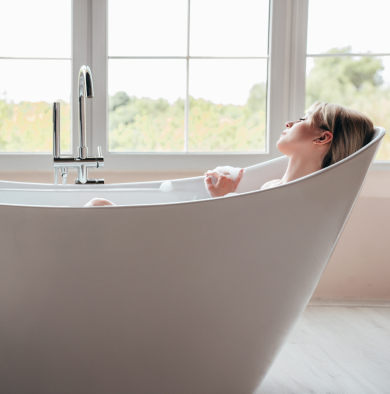 אישה שוכבת בתוך אמבטיה, על רקע חלונות ונוף, אמבטיה בצבע לבן, עיצוב מודרני